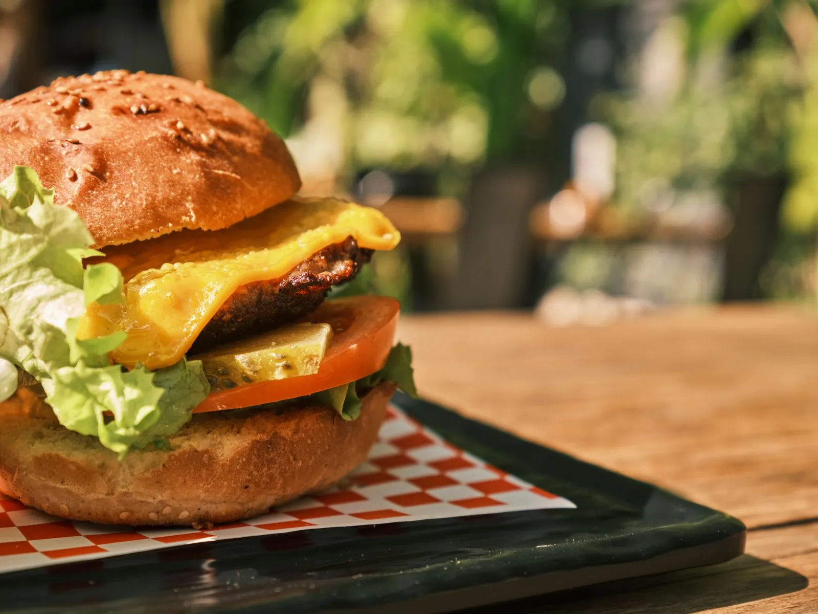 Delicious cheeseburger with lettuce, tomato, and pickles served on a black plate outdoors.